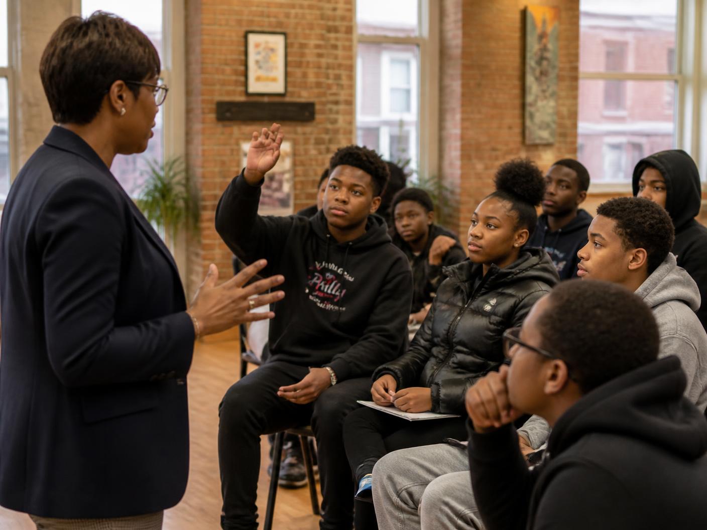 A Black professional speaking with a group of engaged teenagers at a community center